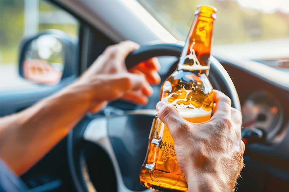 Person holding beer while driving; highlighting the dangers of drinking and driving.