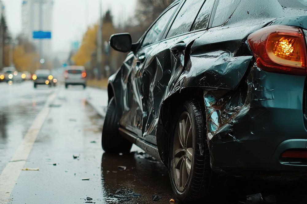 Damaged car with dented side on a wet city road. Traffic is visible in the background.