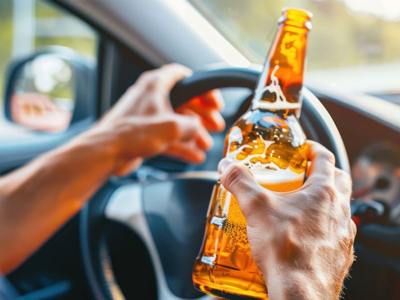 Person holding beer while driving; highlighting the dangers of drinking and driving.