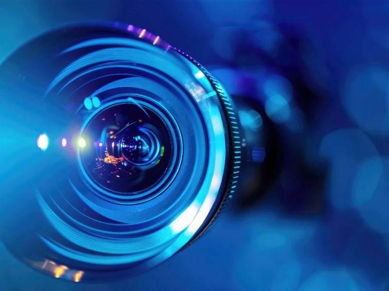 Close-up of a blue camera lens with reflections and a bokeh effect in the background, illustrating photography focus.