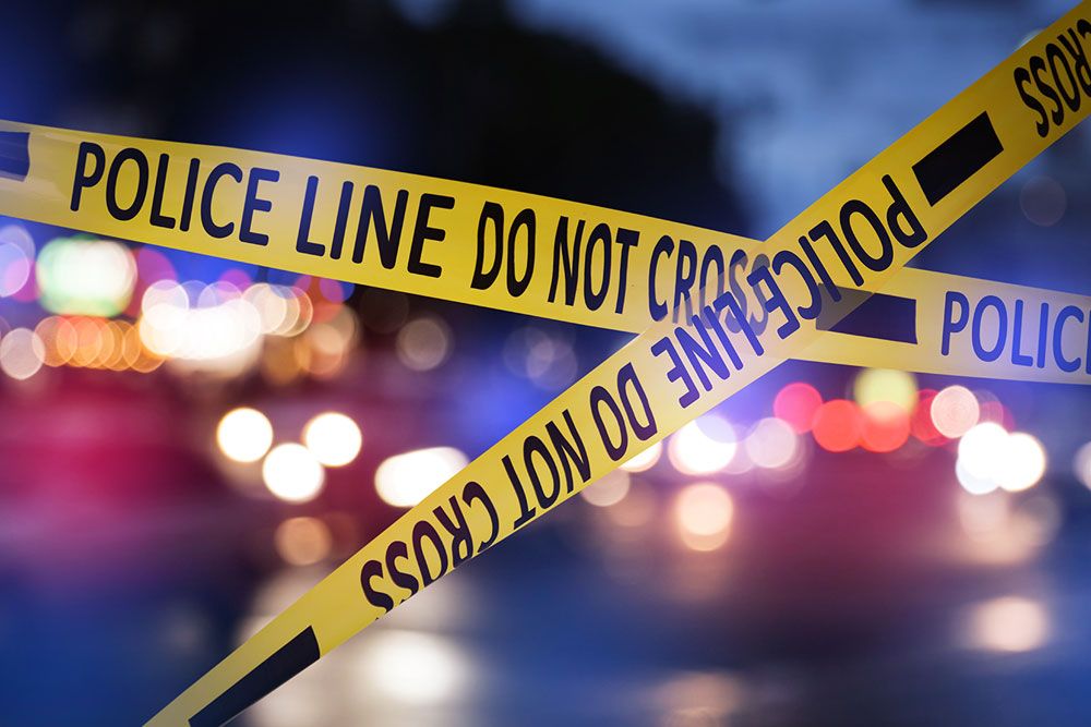 Yellow police line tape blocks area at night with blurred lights in background.