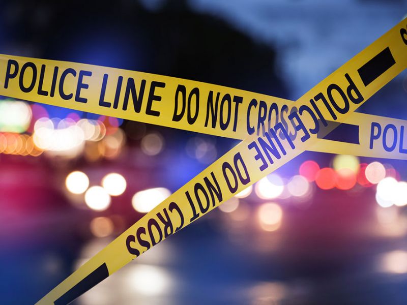 Yellow police line tape blocks area at night with blurred lights in background.