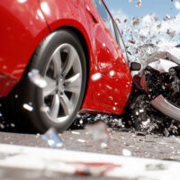 Red car in dramatic collision, front-end damage, and debris flying on urban street under clear sky.