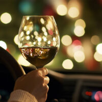 Person holding a wine glass inside a car, with festive lights reflecting.