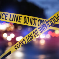 Top-Five-List-to-Do-When-Charged-With-a-Crime Yellow police line tape blocks area at night with blurred lights in background.