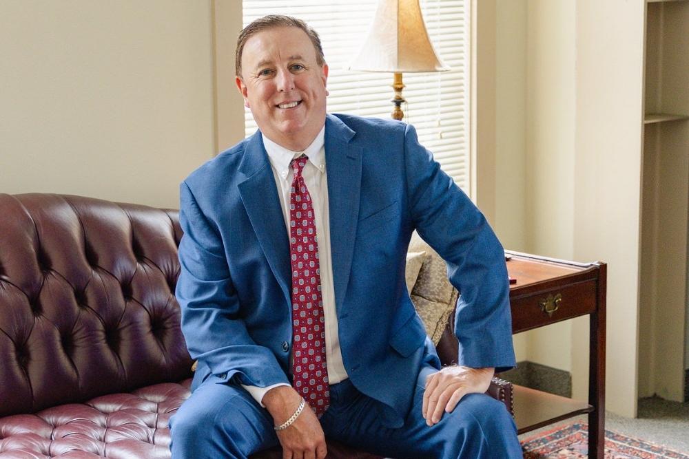 Anthony Montagna III sitting on a couch in a blue suit at his office in Norfolk Virginia